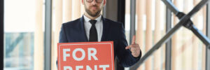 A man holding up a sign that says "For Rent"